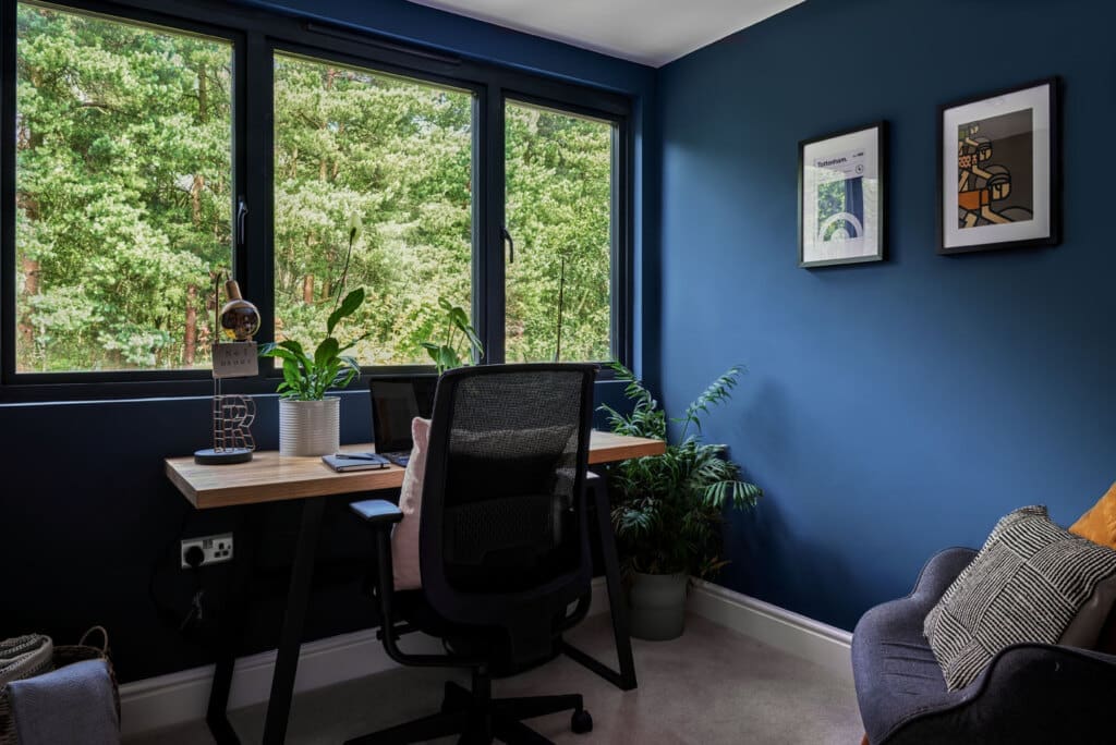 stylish l-shaped loft home office with industrial desk against moody navy walls and windows